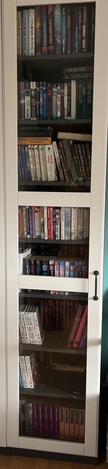 Skříň s prosklenými dveřmi, osm polic s knihami: Zelazny, Sapkowski, Tolkien, Eddings, Gor, Gemmell.